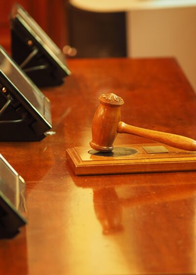 Kuvassa vaalean ruskea pöytä, jonka päällä näkyy vaalean ruskea puinen vasara. Vasaran edessä mustia näyttöjä kolme kappaletta.