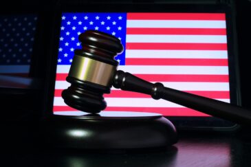 Kuvassa näkyy taustalla Yhdysvaltojen lippu, jossa on sinistä, punaista, sekä valkoisia tähtiä. Kuvan etuosassa on oikeustuomarin vasara.