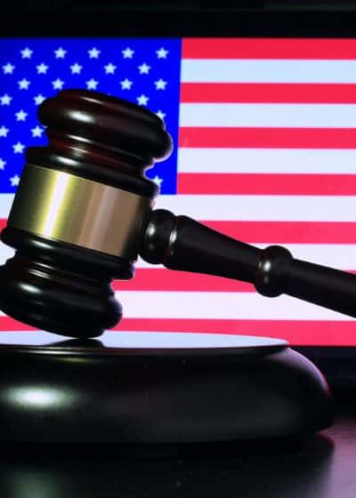 Kuvassa näkyy taustalla Yhdysvaltojen lippu, jossa on sinistä, punaista, sekä valkoisia tähtiä. Kuvan etuosassa on oikeustuomarin vasara.