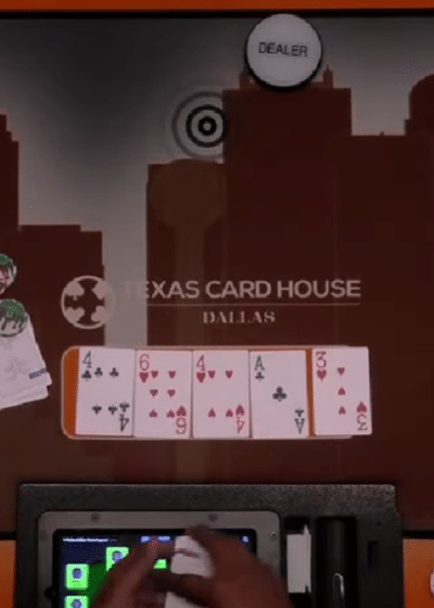 Kuvassa näkyy pelikortteja pokeripelipöydällä, joka on punertava. Pöydässä on talojen kuvia ja pelimerkkejä.