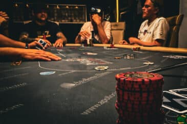 kuvassa näkyy harmaa pöytä, jossa on pokerimerkkejä. Taustalla näkyy ihmisiä, heillä on vaaleita ja tummia paitoja.