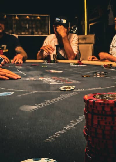 kuvassa näkyy harmaa pöytä, jossa on pokerimerkkejä. Taustalla näkyy ihmisiä, heillä on vaaleita ja tummia paitoja.