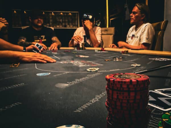 kuvassa näkyy harmaa pöytä, jossa on pokerimerkkejä. Taustalla näkyy ihmisiä, heillä on vaaleita ja tummia paitoja.