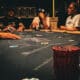 kuvassa näkyy harmaa pöytä, jossa on pokerimerkkejä. Taustalla näkyy ihmisiä, heillä on vaaleita ja tummia paitoja.