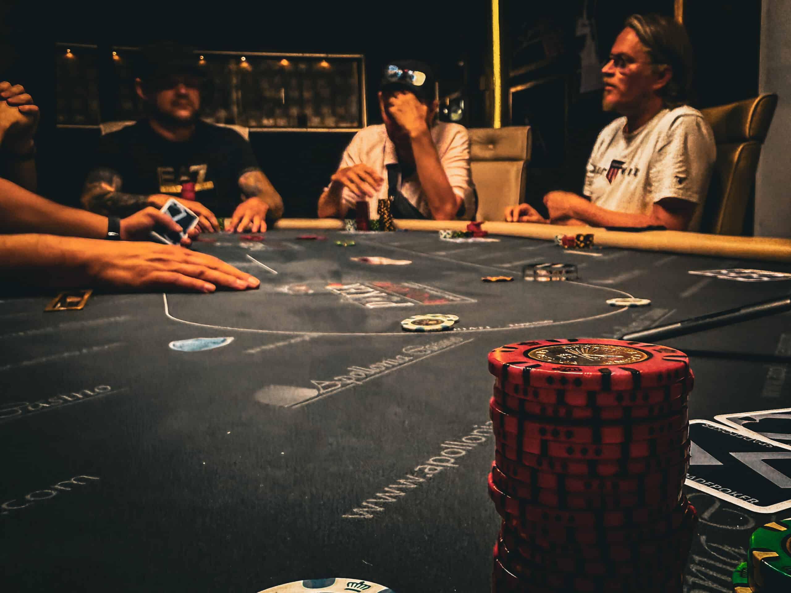 kuvassa näkyy harmaa pöytä, jossa on pokerimerkkejä. Taustalla näkyy ihmisiä, heillä on vaaleita ja tummia paitoja.
