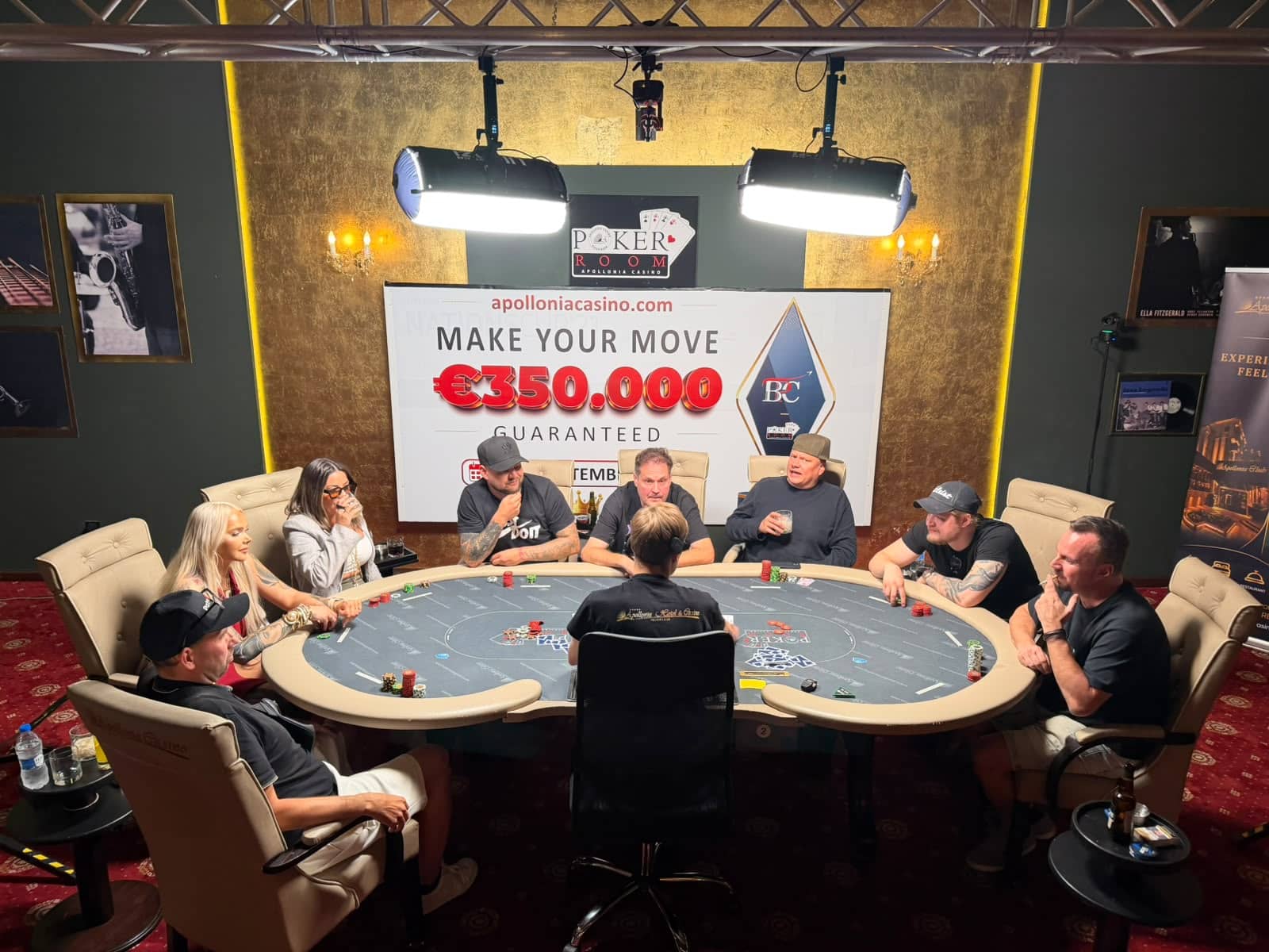 Kuvassa näkyy useita ihmisiä pokeripöydän äärellä. Taustalla on iso taulu, jossa numeroita ja seinät ovat vihreät ja keltaiset